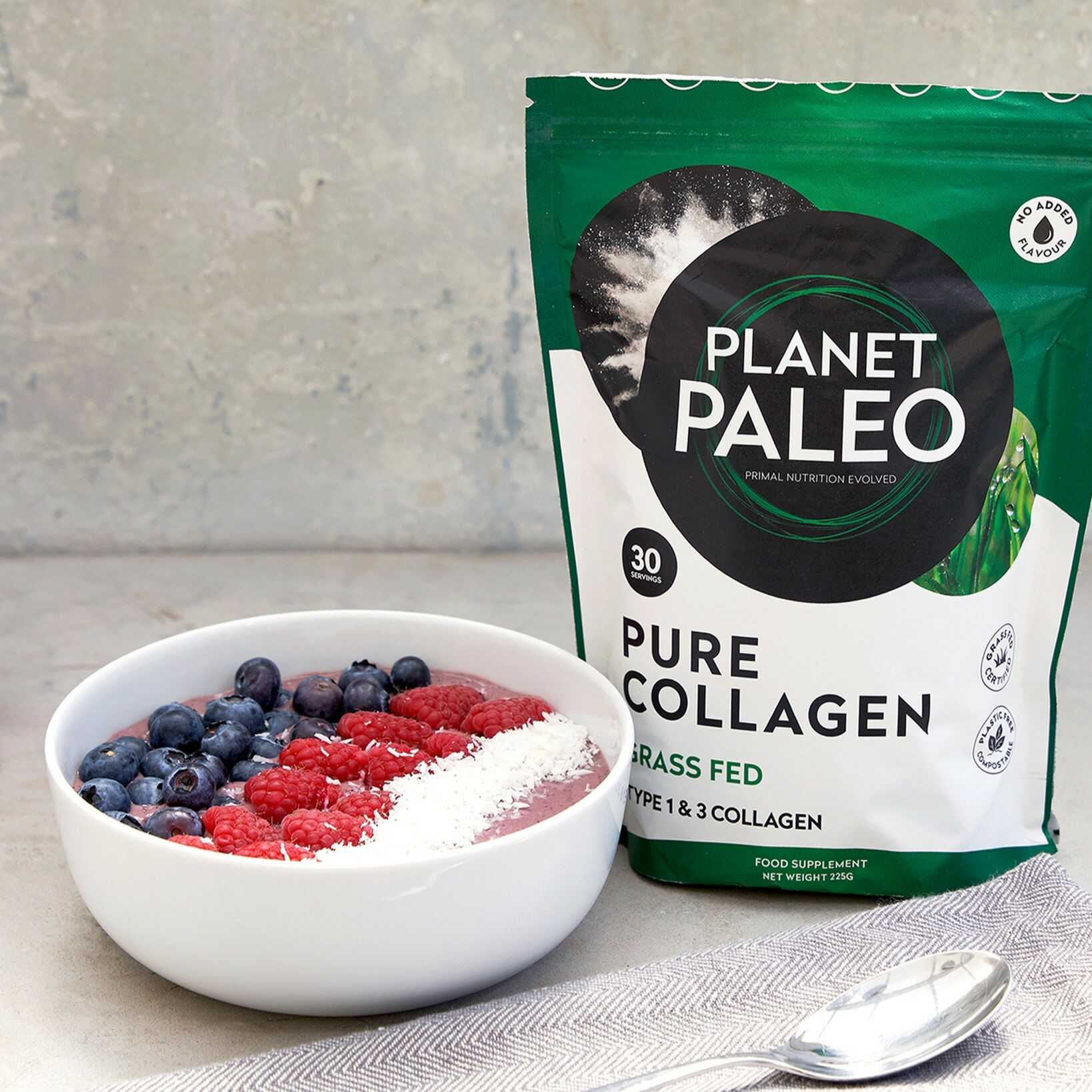 Planet Paleo Pure Collagen grass-fed pouch standing beside a smoothie bowl topped with blueberries, raspberries and shredded coconut on a light kitchen surface.